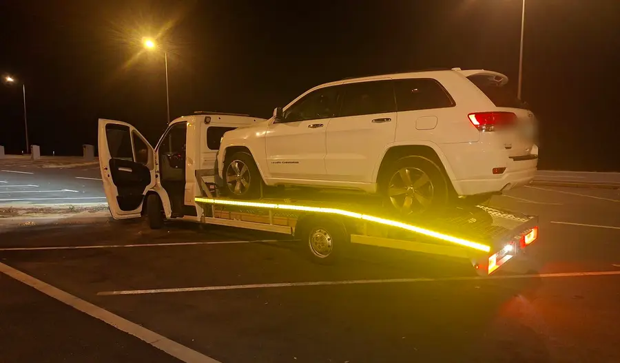 Kamion AUTO MIRO s utovarenim SUV-om noću